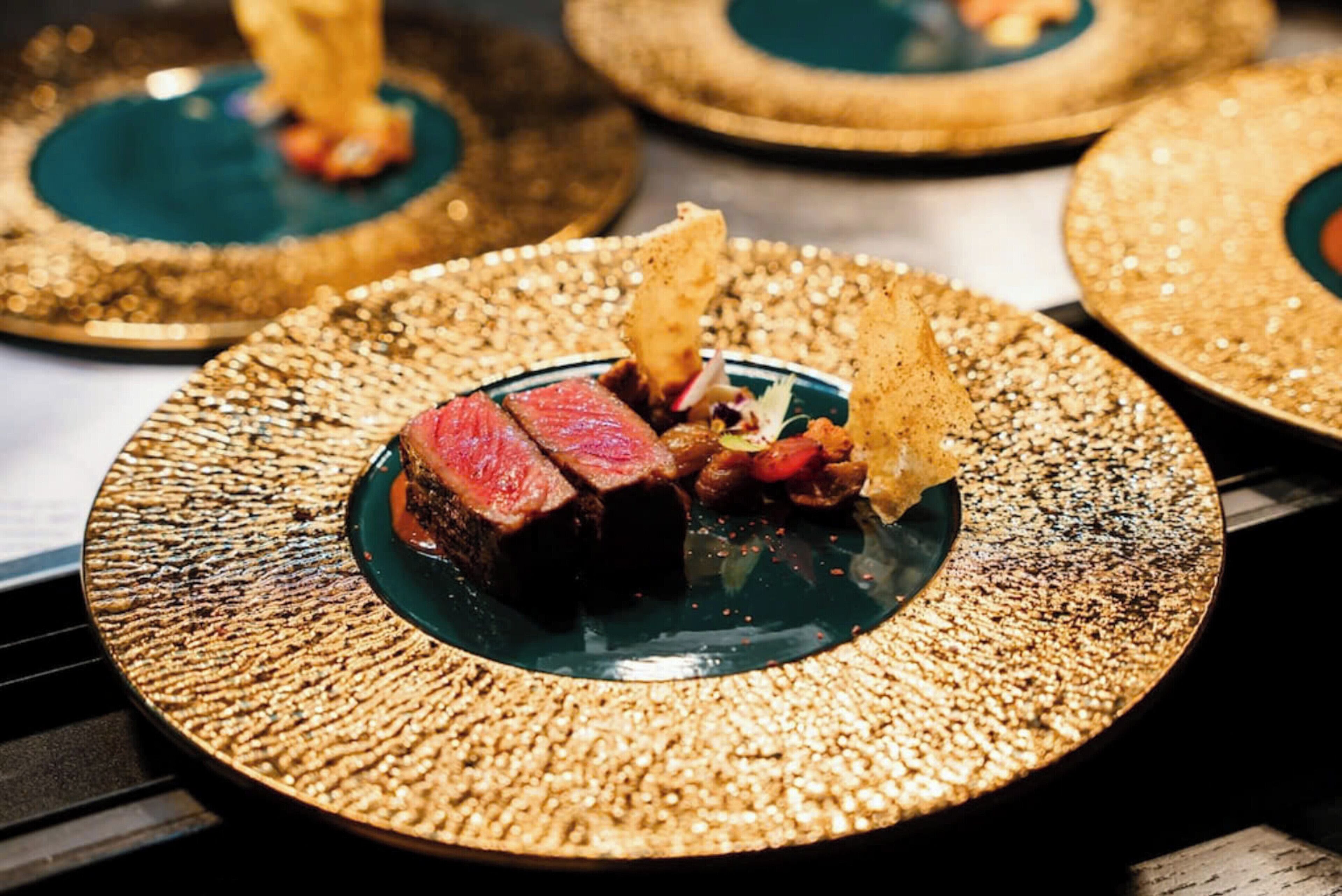 A plate of steak with vegetables and chips on a textured golden plate.