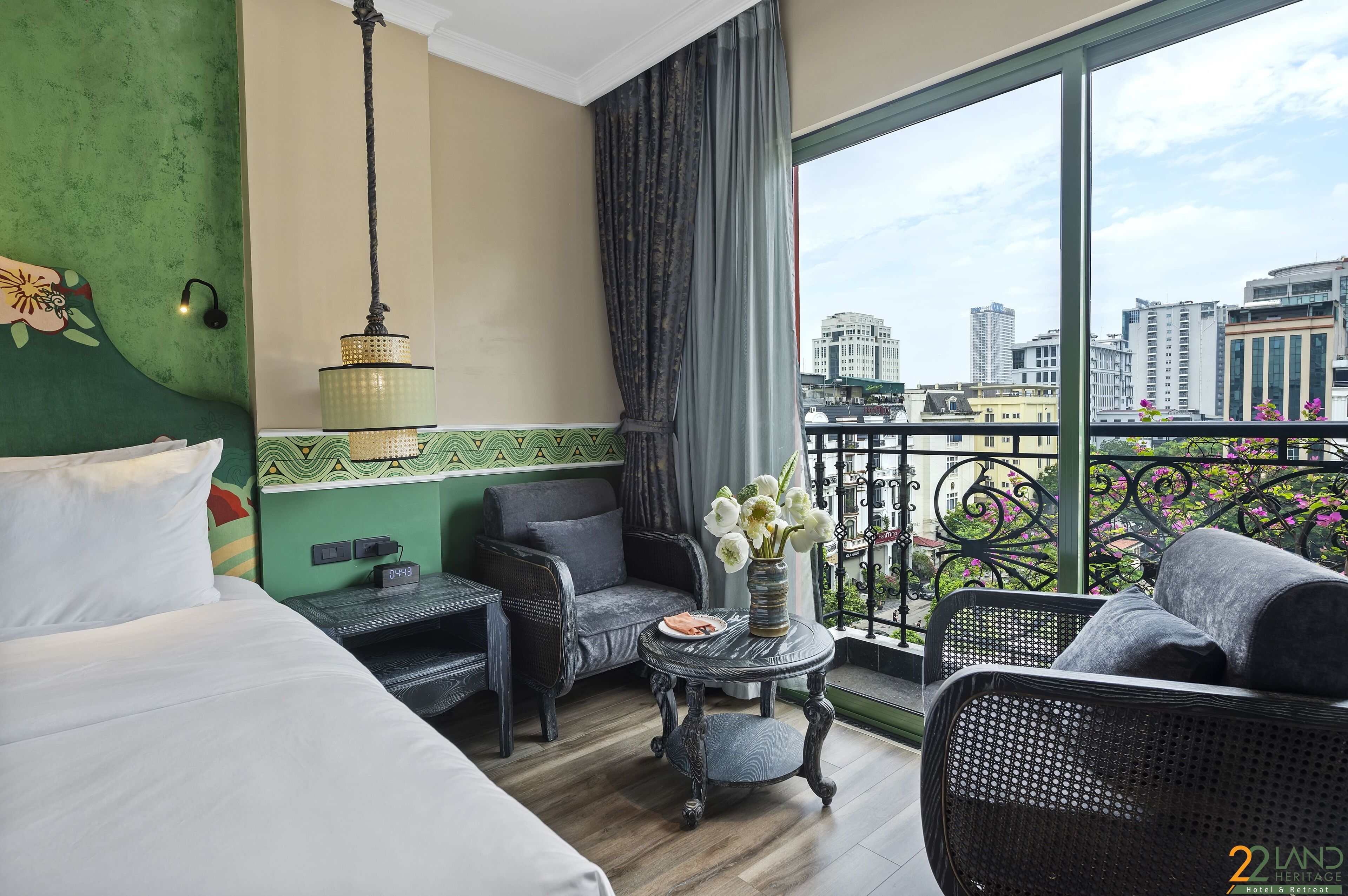 Et hotelværelse med seng, sofa, et lille bord med blomster og en balkon med udsigt over byen.