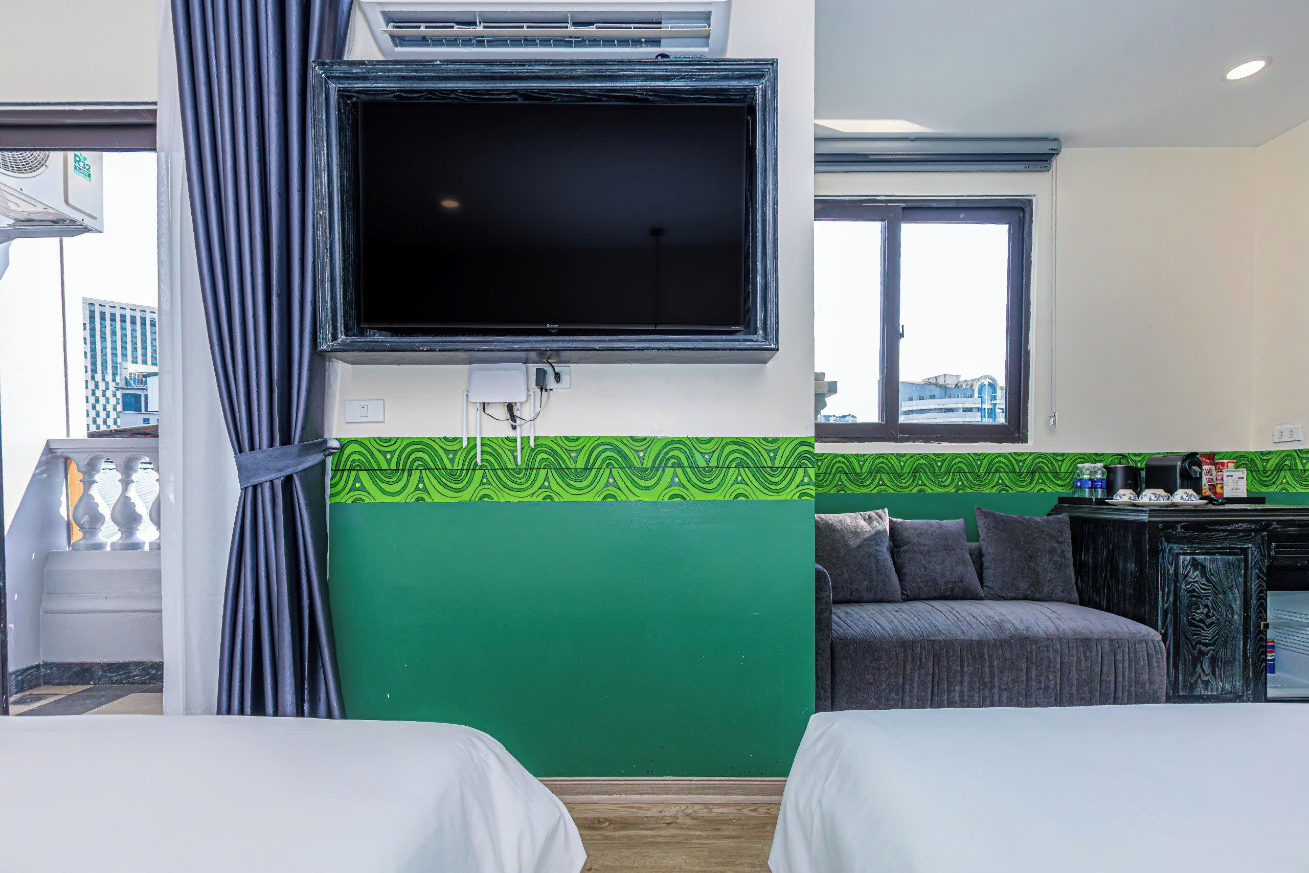 Habitación de hotel con dos camas, un televisor montado en la pared, una pared verde decorativa, una ventana y vistas al exterior.