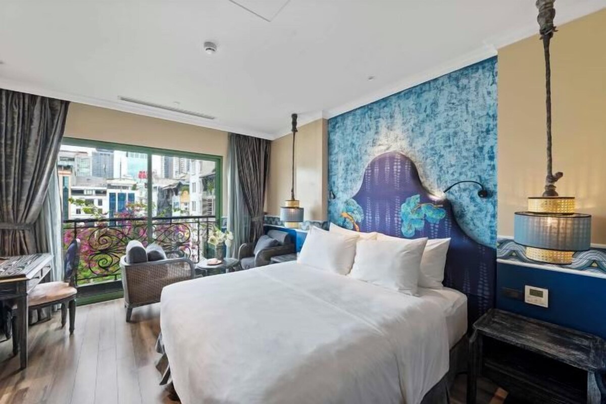 A hotel room with a large bed, a view of the city through a balcony, and a decorative headboard.