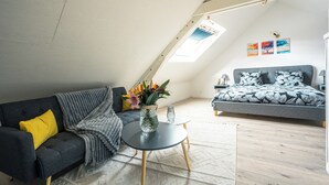 A loft-style bedroom with a sloped ceiling, a bed with patterned bedding, a gray sofa with a yellow pillow, and a small table with a vase of flowers. - An enchanting townhouse, a unique experience! (Nozay)