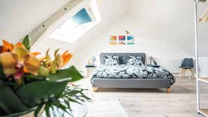 A bedroom with a sloped ceiling, a bed with a leaf-patterned bedspread, a small window, and wall art. - An enchanting townhouse, a unique experience! (Nozay)