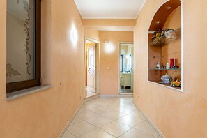 A hallway with a tiled floor, a door leading to a bathroom, and a shelf with decorative items. - GuestHost - Comfortable 80 sqm apartment in Aci Catena, located on the third floor without an elevator. Equipped with WiFi, air conditioning, and a large terrace ideal for outdoor relaxation. Aci Catena is a quiet Sicilian town rich in history and cultur (Aci Catena)