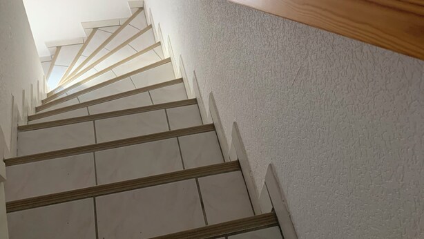 Una escalera con paredes blancas y barandales de madera que sube.