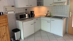 Una cocina compacta con armarios blancos, un microondas, una cafetera y un lavabo.
