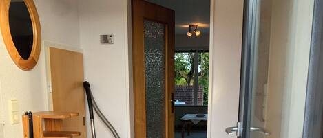 Ein heller, moderner Flur mit einer Holztreppe, einem Staubsauger und einer Glastür zu einem Außenbereich.