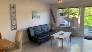 Una sala de estar acogedora con un sofá de cuero negro, una mesa de madera con mantel floreado y un ventanal con vistas a un jardín.