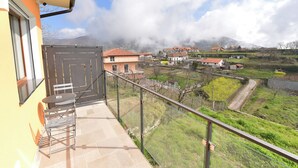 Uma varanda com mesa e cadeiras, com vista para uma aldeia com casas e uma montanha ao fundo.