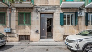 A building with a dark entrance door, green shutters, and a parked white car. - GuestHost - Stylish City Living in Central Catania (Catania)