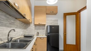 A kitchen with a black refrigerator, wooden cabinets, a double sink, and a tiled backsplash. - GuestHost - Stylish City Living in Central Catania (Catania)