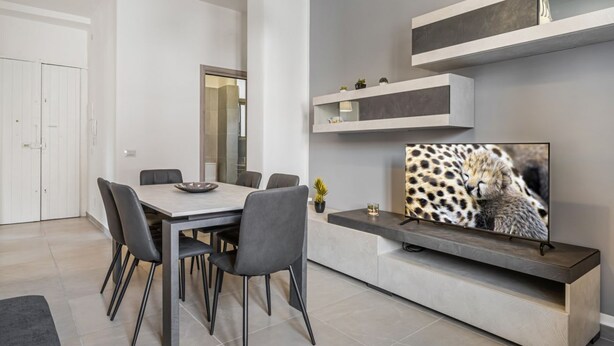 A modern dining area with a table and chairs, a built-in TV, and a minimalist design. - GuestHost - Stylish City Living in Central Catania (Catania)