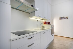 Une cuisine moderne avec des meubles blancs, un évier en acier inoxydable et un four encastré.
