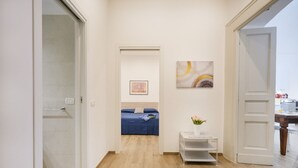 Ein Flur, der zu einem Schlafzimmer führt, mit einem Bett, einem kleinen Tisch mit einer Vase und Bildern an der Wand.
