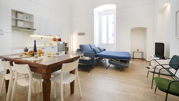 Ein modernes, gut beleuchtetes Zimmer mit Essbereich, einem Bett und einem Fernseher.