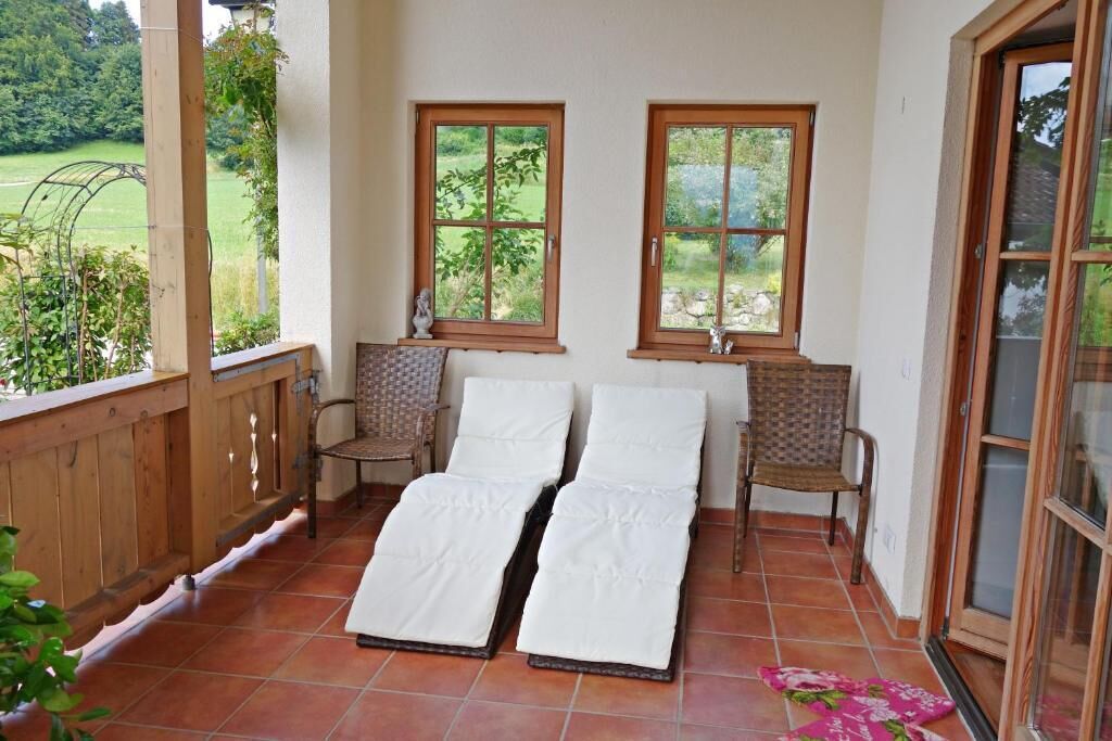 Ein sonnendurchfluteter Raum mit zwei Liegestühlen, einem Holgitter und Blick auf einen Garten.
