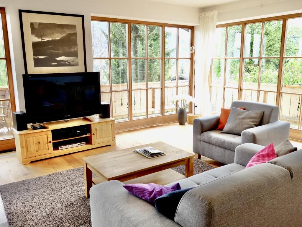 Een woonkamer met een televisie, bank en grote ramen.