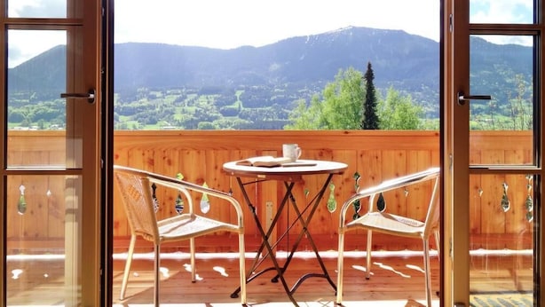 Eine Holzterrasse mit Tisch und zwei Stühlen, die einen Blick auf eine gebirgige Landschaft bietet.