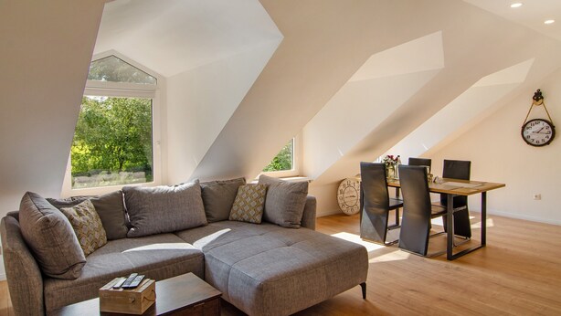 Ein Loft-Zimmer mit Ecksofa, Esstisch und Stühlen sowie einer großen Wanduhr.