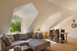 Un espacio tipo loft con un sofá seccional, una mesa de comedor con sillas y un reloj grande en la pared.