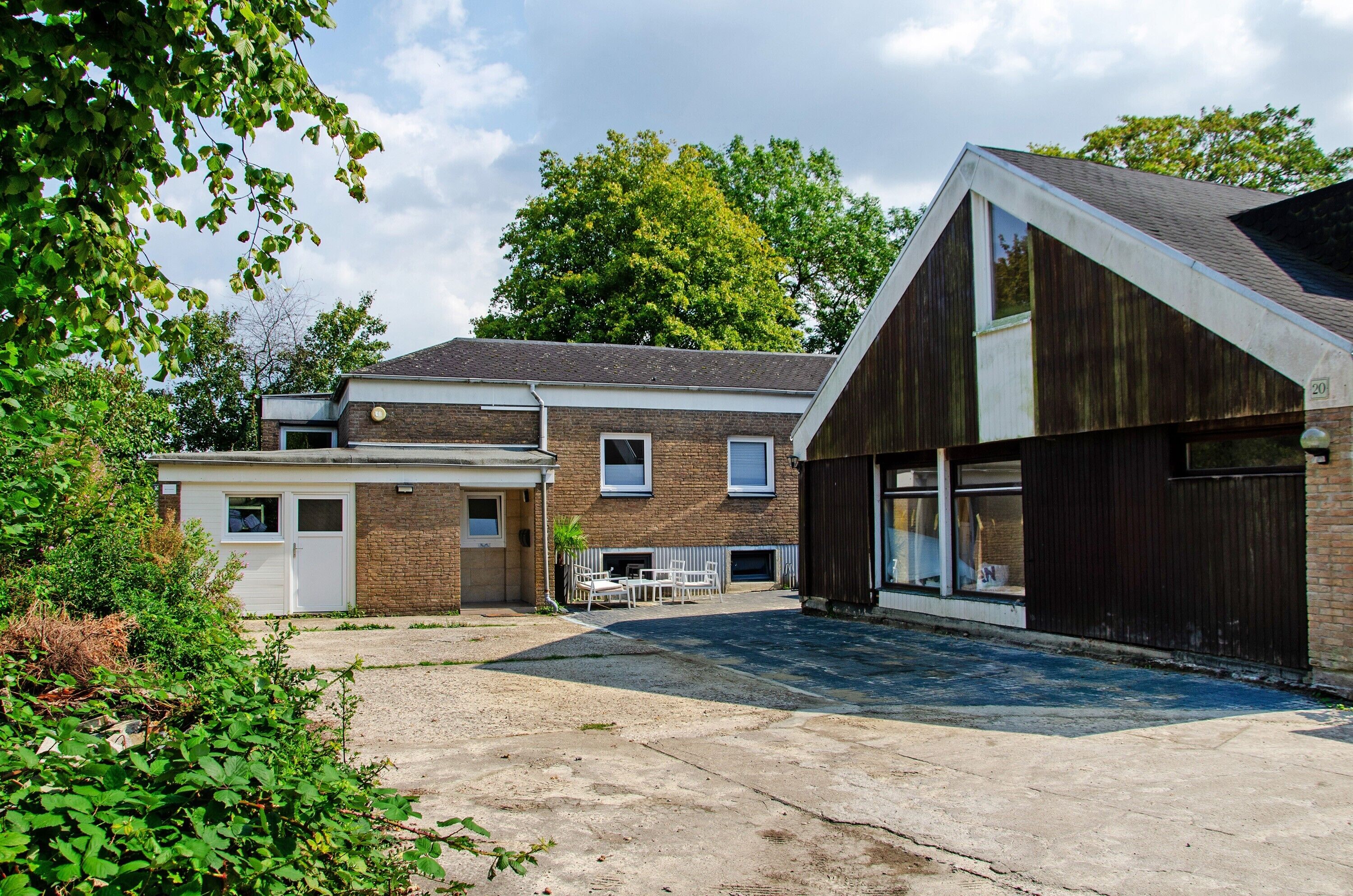Ein Gebäude mit Backsteinfassade, einer Garage und einer überdachten Außenbereich mit Tisch und Stühlen.