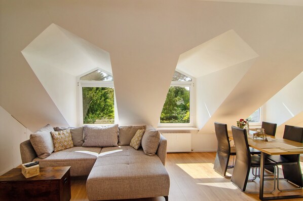 A modern loft with a sectional sofa, dining table, and chairs, large windows, and a sloped ceiling.
