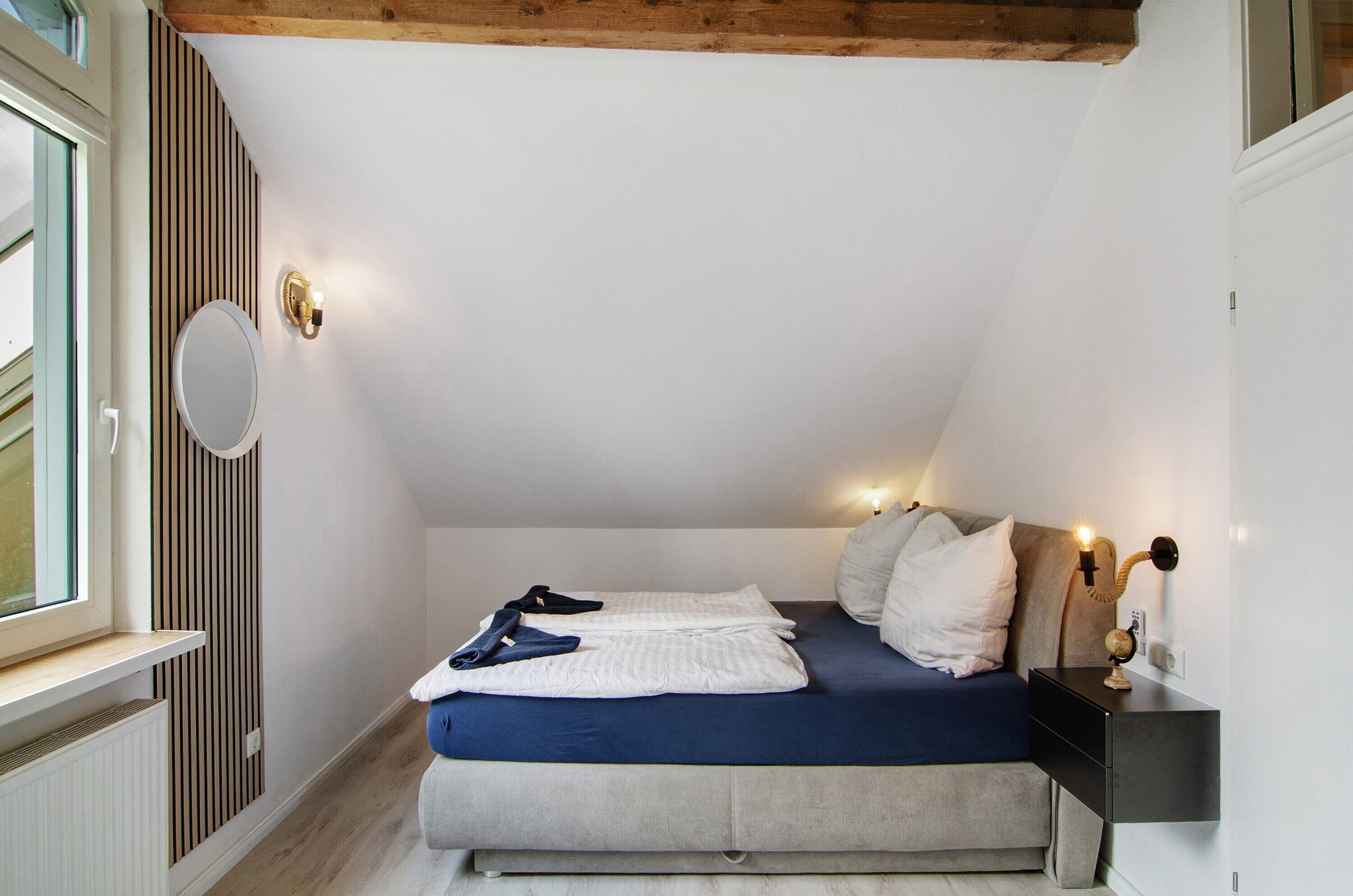 Un dormitorio con cama, mesita de noche, luz empotrada en la pared y ventana.