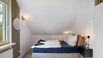 Un dormitorio con cama, mesita de noche, luz empotrada en la pared y ventana.
