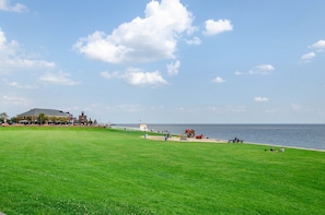 A grassy field with a beach, a building with a red roof, and a lighthouse in the distance.