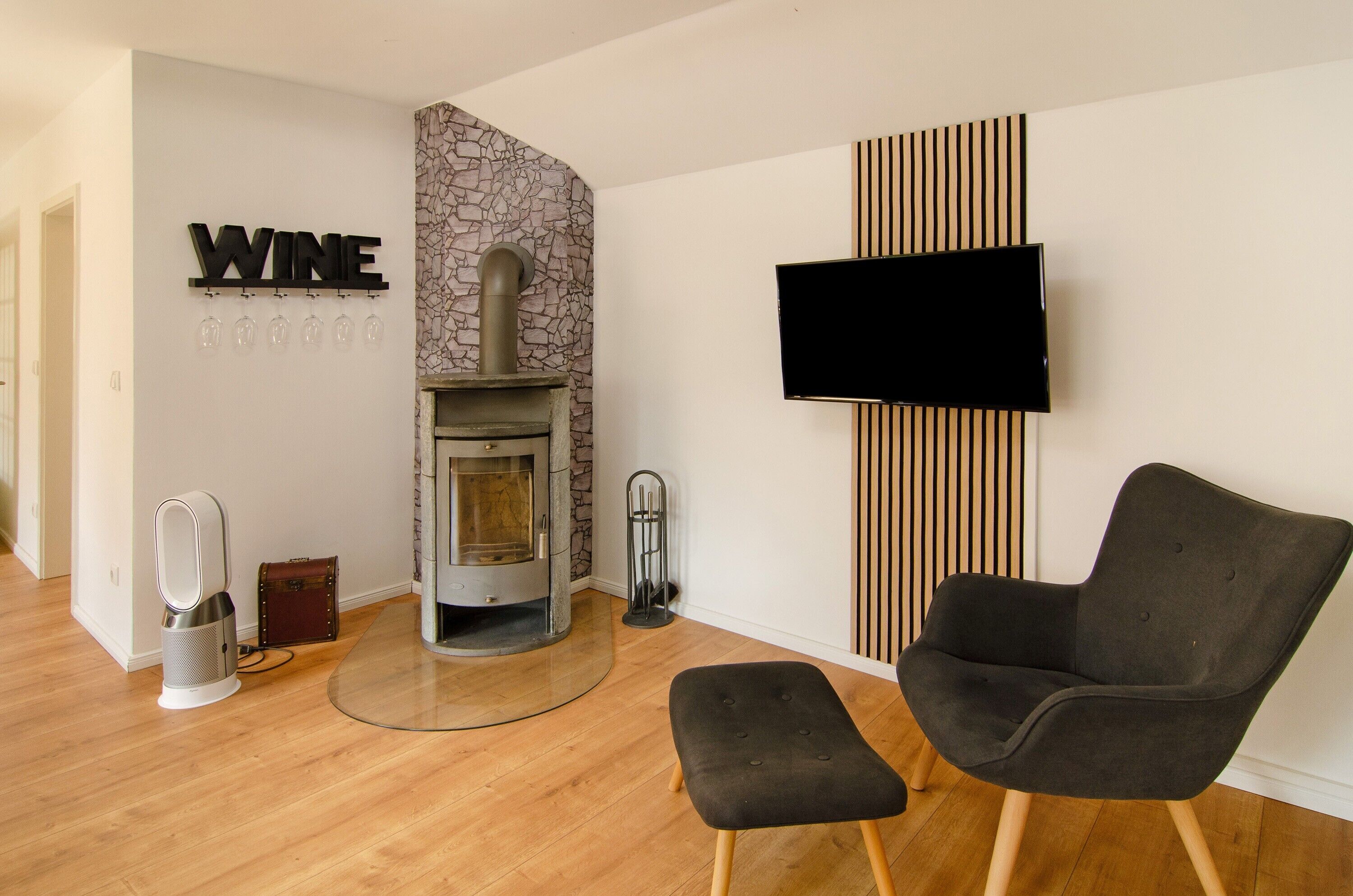Een moderne woonkamer met een open haard, een wandtelevisie, een zwarte fauteuil en een klein voetenbankje.