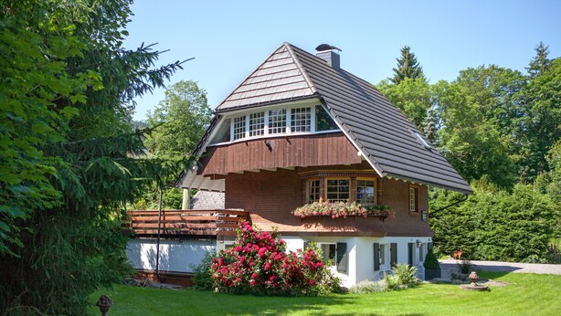 Una casa con techo inclinado, una chimenea y un pequeño porche con un macetero.