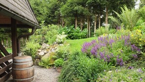 Un jardín con una estructura de madera, un sendero de grava y diversas plantas y flores.