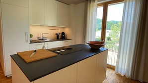 A modern kitchen with a large island, a sink, and a view of greenery outside.