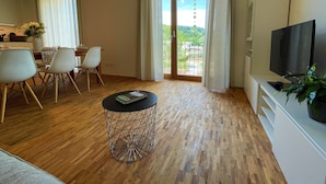 A modern living room with a dining area, a TV, and a balcony with a view.
