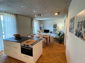 A modern kitchen with an island, dining area with a table and chairs, a TV, and a bookshelf.