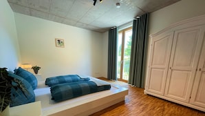 A bedroom with a bed, a nightstand, a lamp, a window with curtains, and a wardrobe.