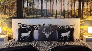 Een slaapkamer met een boswanddecoratie, beddengoed met een patroon en drie kussens met hertenmotief.