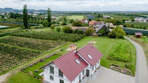 Una casa grande con techo rojo, rodeada por un jardín cuidado y campos.