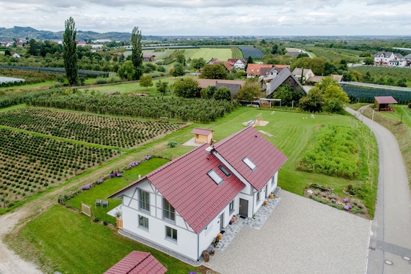 Une grande maison avec un toit rouge, entourée d’un jardin bien entretenu et de champs.