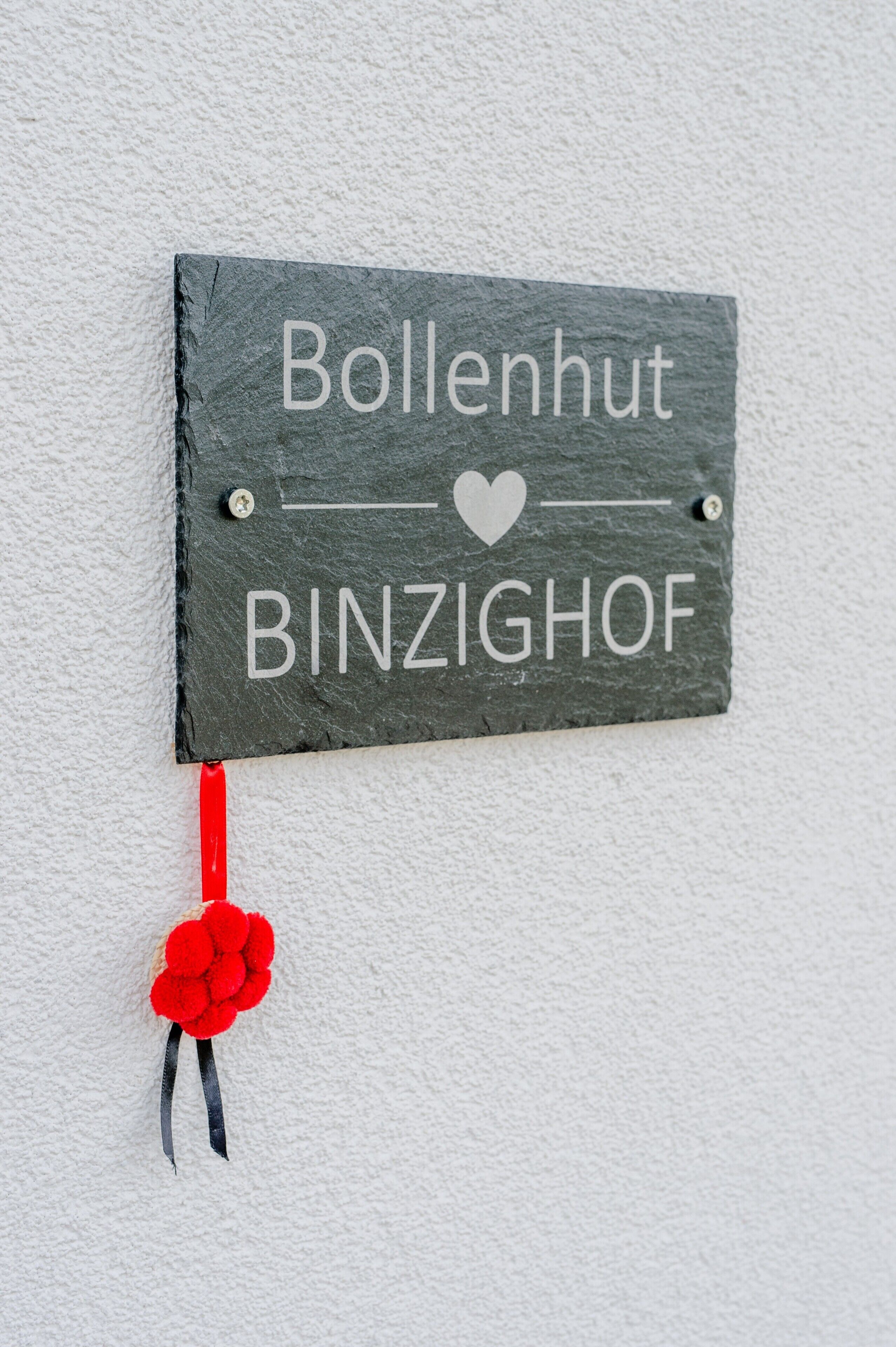 Ein Schilt mit dem Text 'Bollenhut BINZIGHOF' und einer roten Blütenverzierung.