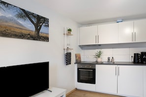 Una cocina moderna con armarios blancos, un horno negro y un televisor de pantalla plana sobre un pedestal blanco.
