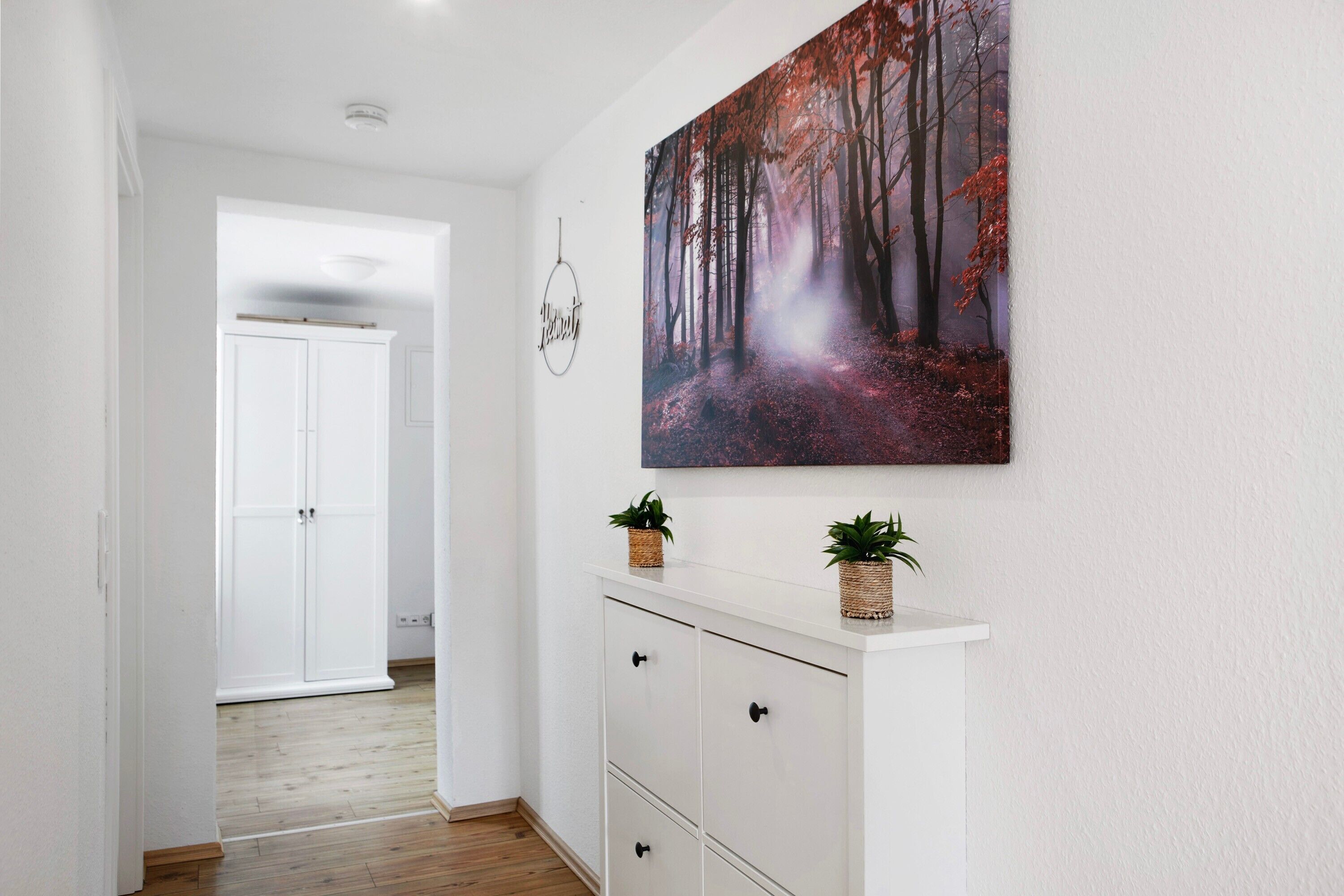 A hallway with a white cabinet, a painting of a forest, and a door in the background.