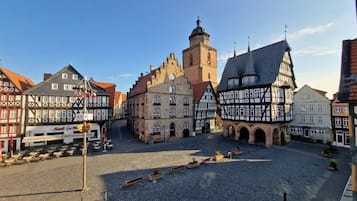 Ein Kopfsteinpflasterplatz mit traditionellen Fachwerkhäusern, einem Glockenturm und blauem Himmel.
