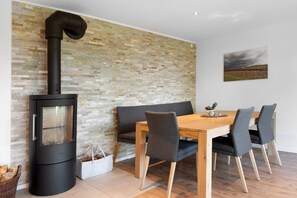 A modern interior with a wood-burning stove, a dining table with chairs, a bench, and a stone-patterned wall.