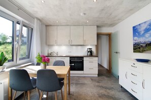 A modern kitchen with a dining area, large windows, and a painting on the wall.