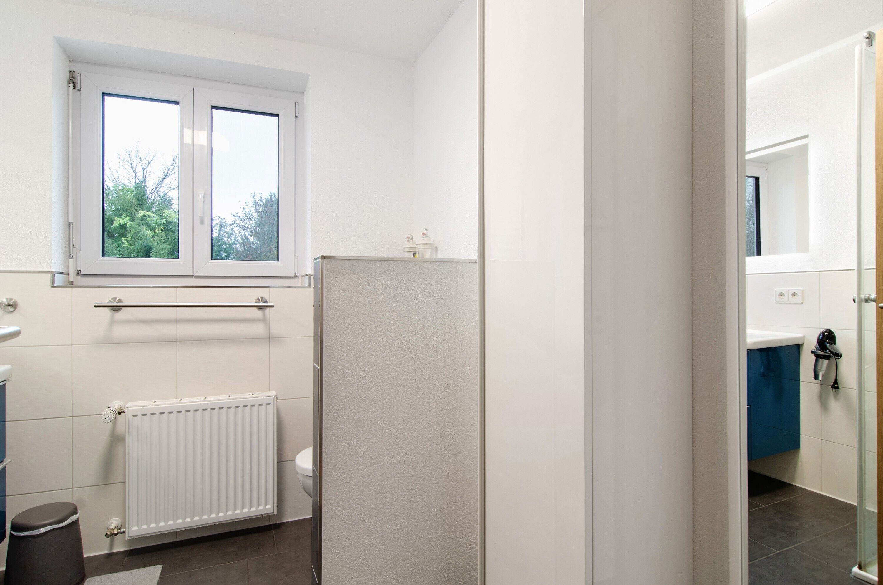 A bathroom with a window, a radiator, a toilet, and a shower area.