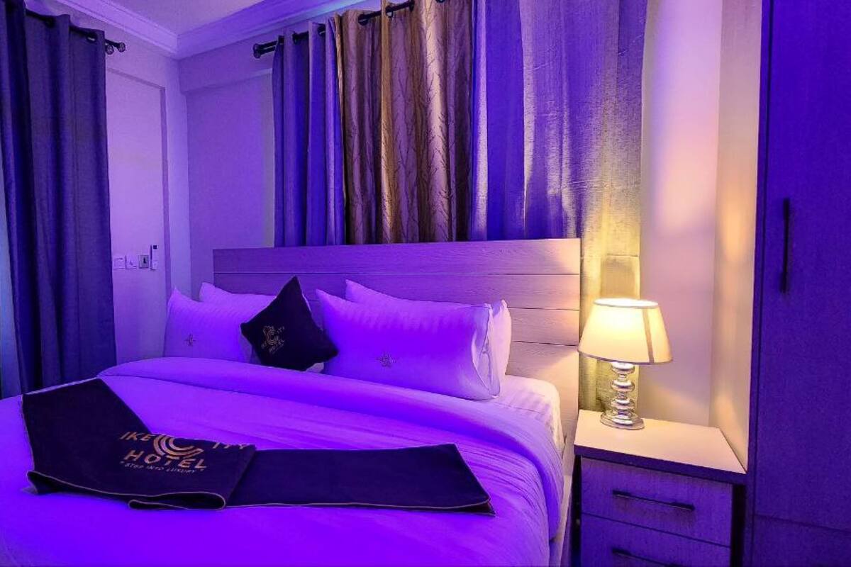Une chambre d’hôtel avec un lit, des rideaux, une table de chevet avec une lampe et un panneau sur le lit.