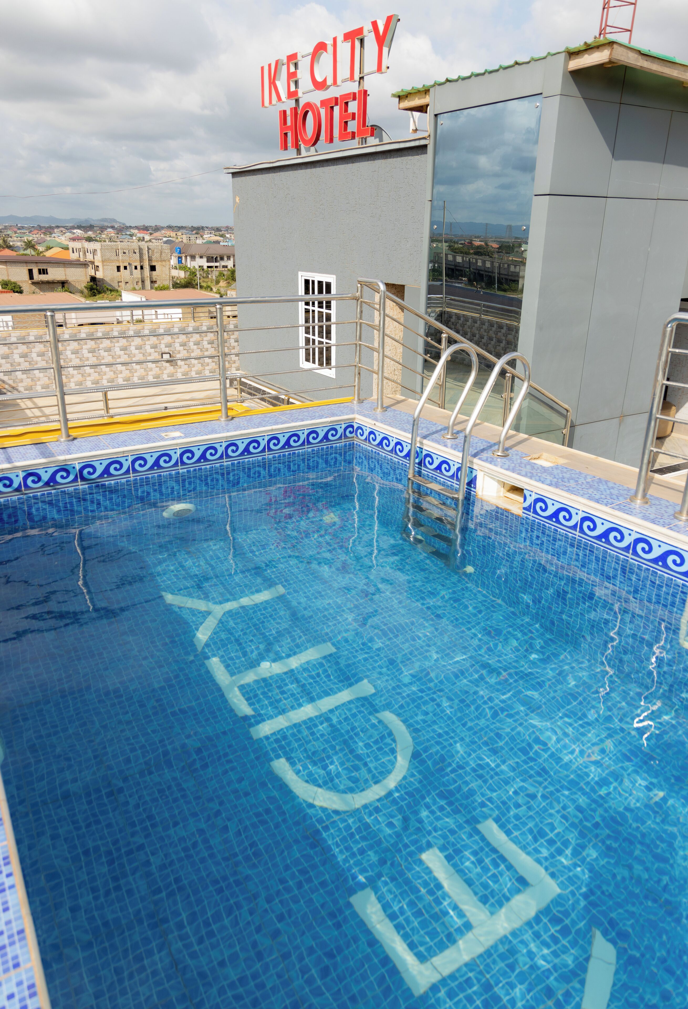 A swimming pool with a blue tiled border and a sign for "IKE CITY HOTEL" above it.