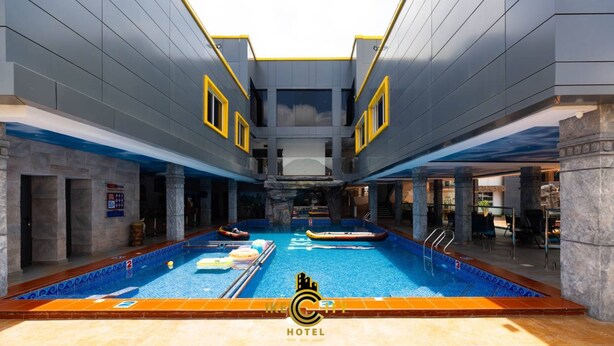 A large indoor swimming pool with a modern design, surrounded by stone pillars and a stone wall. - IKE CITY Hotel (Tema)