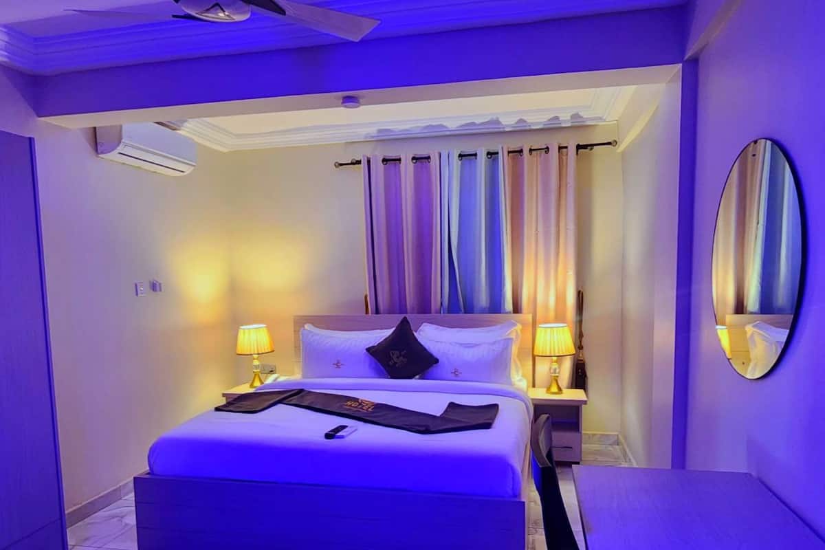 Une chambre d’hôtel moderne avec un grand lit, deux lampes de chevet, un ventilateur de plafond et un grand miroir au mur.