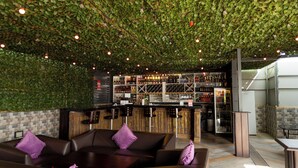 A bar area with a green leafy ceiling, wooden bar counter, and seating with purple cushions. - IKE CITY Hotel (Tema)